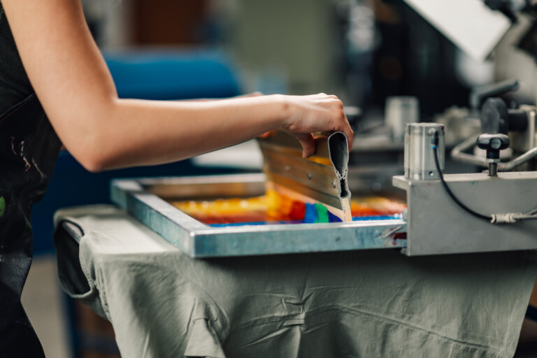 Close up of graphic worker's hands with squeegee silkscreen printing.